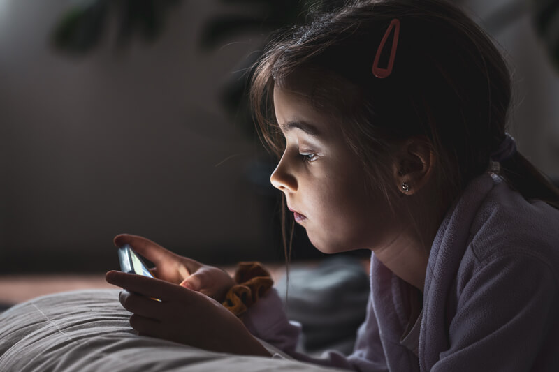 little girl uses smartphone lying pillow home